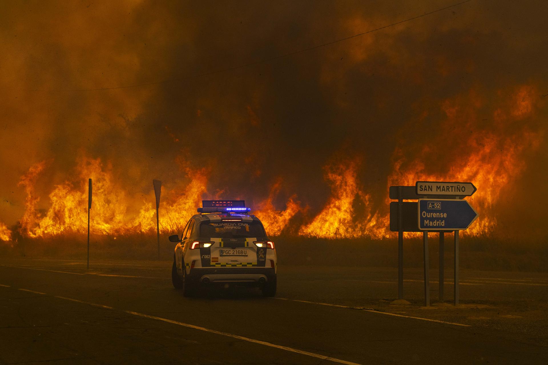 Un vehículo da Garda Civil recúa ante o incendio no acceso á autovía Ourense–Madrid, en Cualedro, Galicia. – Brais Lorenzo